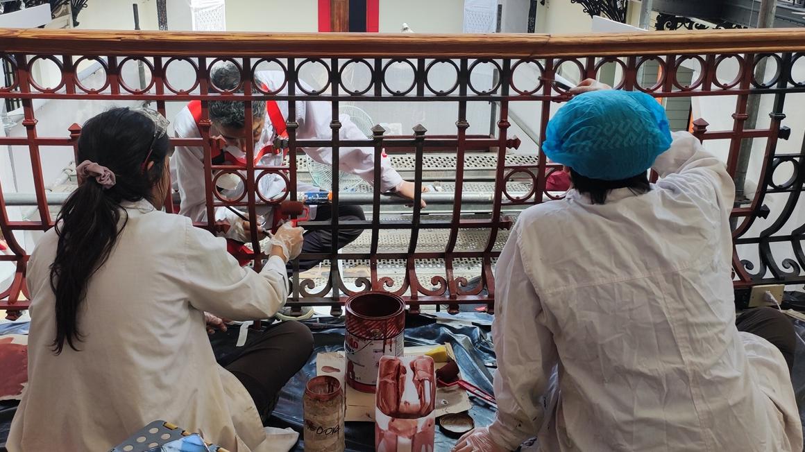 Fotografía de tres personas con batas blancas, trabajando en las rejas de los balcones 