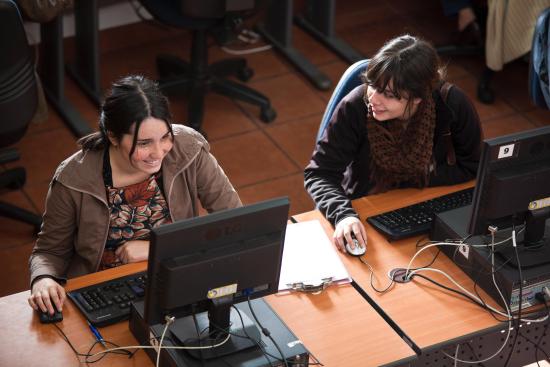 Dos mujeres están sentadas frente a computadores realizando cursos.